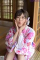 A woman in a pink and white kimono sitting on a wooden floor.